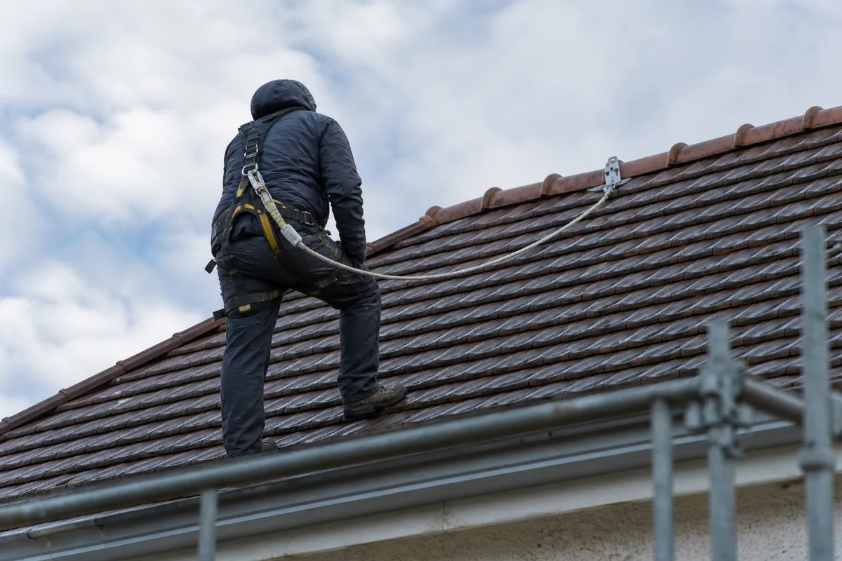 Couvreur harnaché sur un versant de toiture, ligne de vie ancrée au faîtage, échafaudage en pied de mur