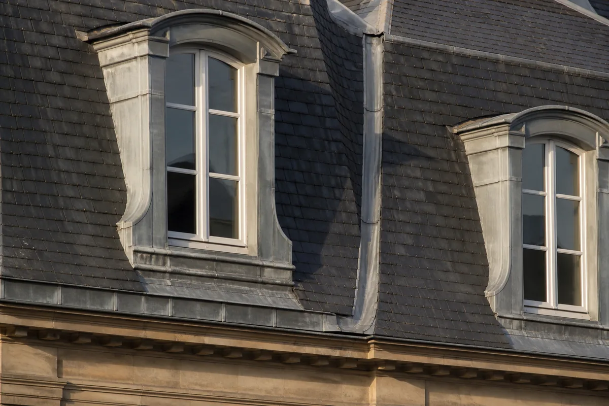 Toiture en ardoise d’une demeure bourgeoise de Fontainebleau avec lucarnes et chéneau de zinc sous une lumière rasante